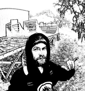 Black and white photo of Matt the ramp builer, in a black sweatshirt with a miniramp build in the background