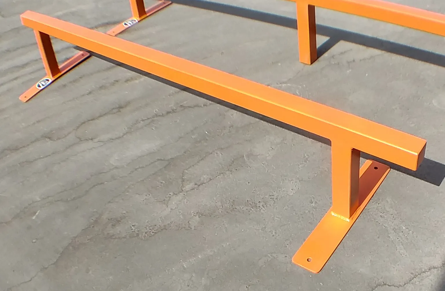 Two orange flat bar skate rails side by side, one foot high by six foot long and one foot high by eight foot long