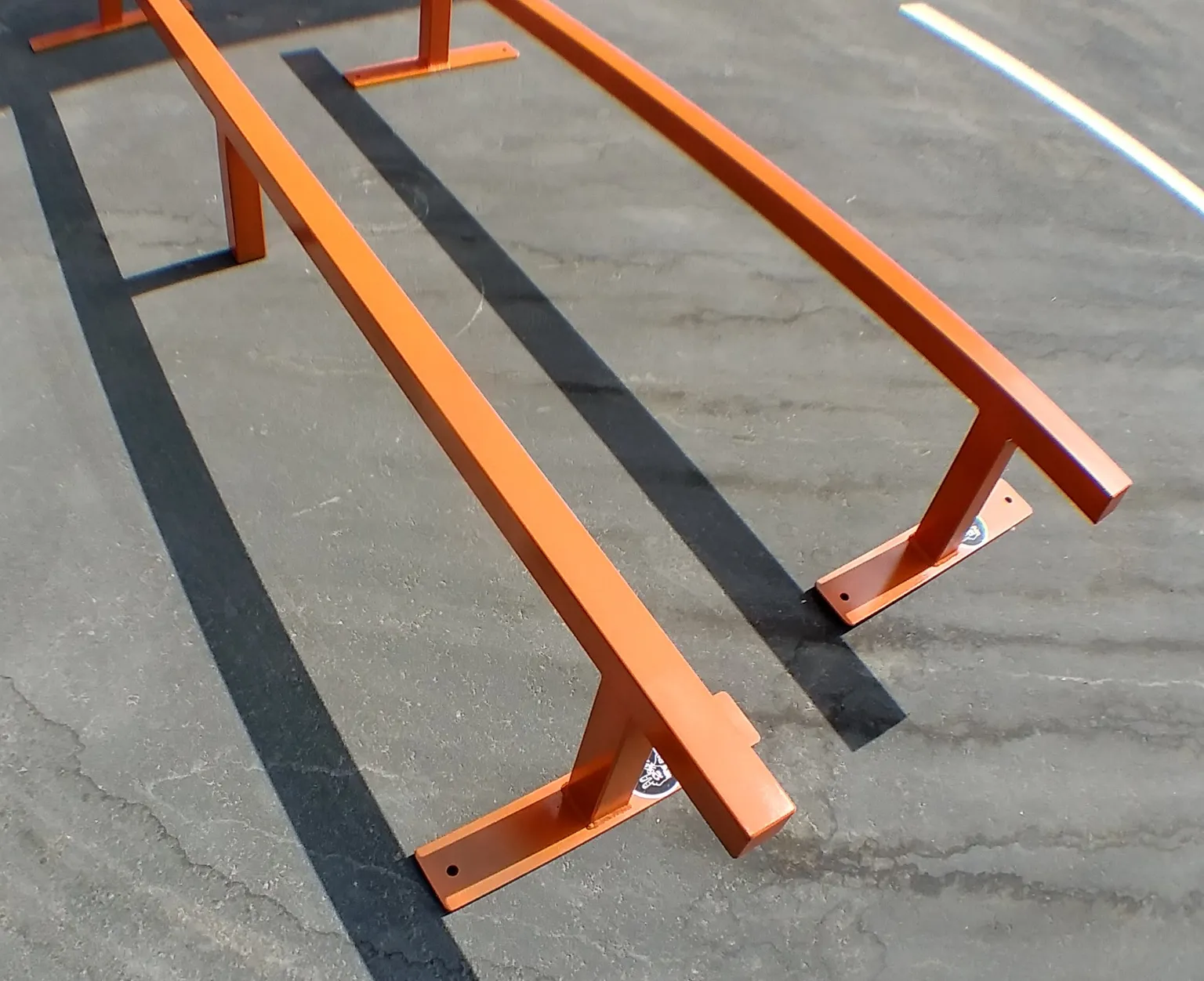 Two orange flat bar skate rails side by side, one foot high by six foot long and one foot high by eight foot long, secondary angle