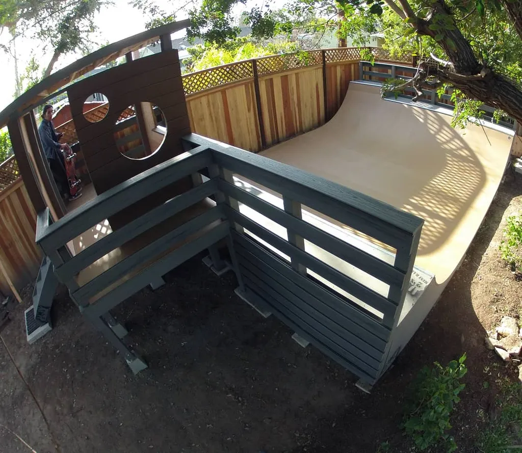 Four foot high by sixteen foot wide miniramp with custom deck railing and platform with tree overhead by wooden fence